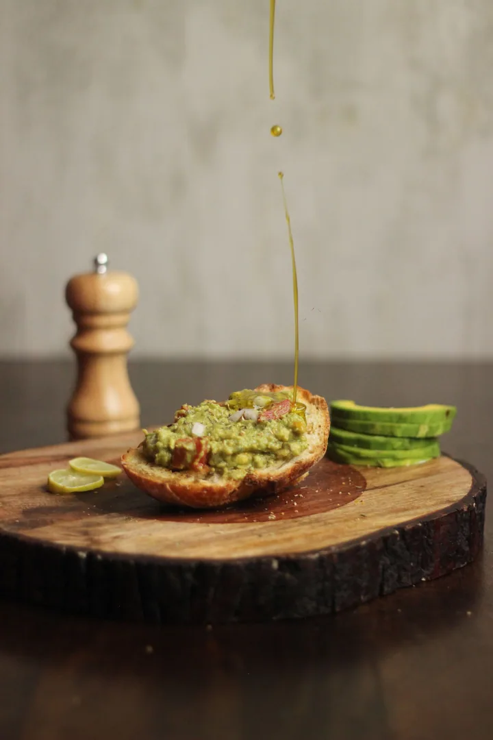 Toast topped with smashed avocado, drizzled with oil, on a wooden board