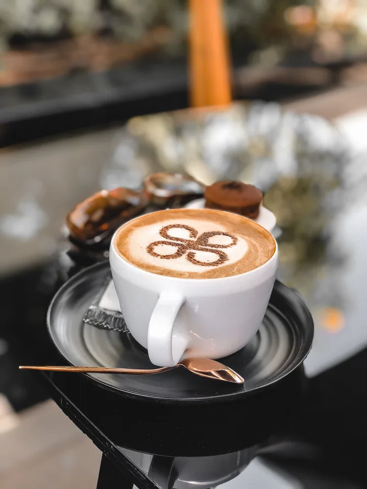 White cup of milky coffee with a cocoa pattern on a black saucer