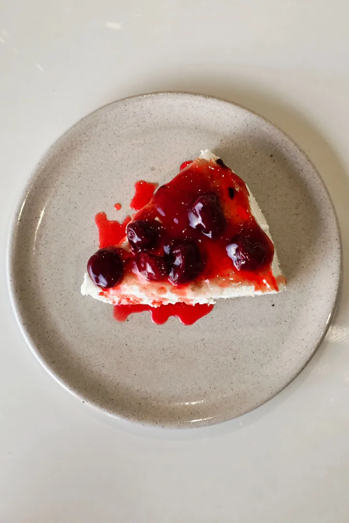 Slice of cheesecake topped with cherries on a speckled plate