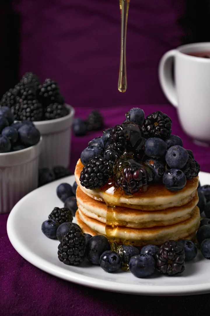 Stack of pancakes with blueberries, blackberries and syrup on a white plate