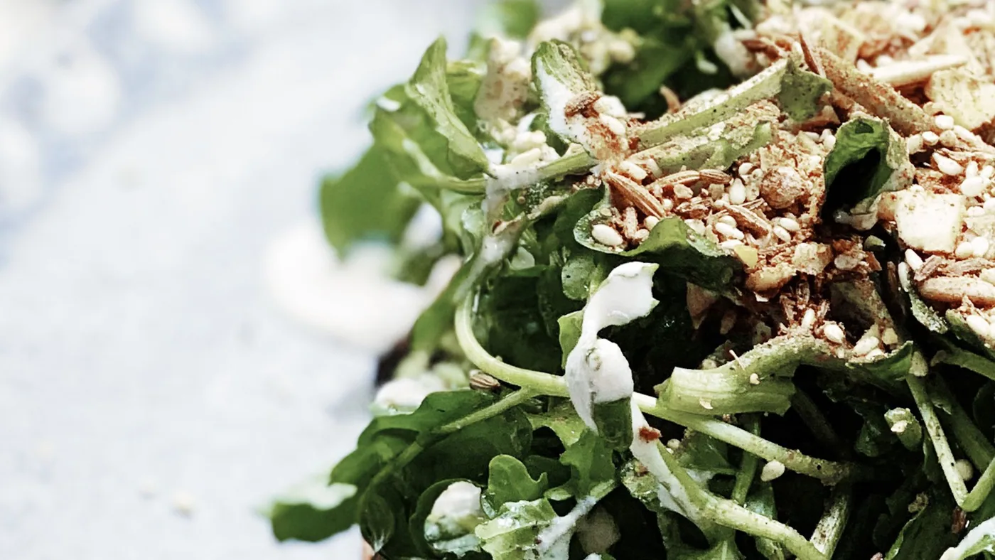 Close-up of rocket leaves topped with seeds and a creamy dressing